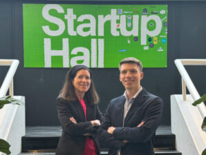 A man and woman stand in front of a green sign with white text that reads Startup Hall